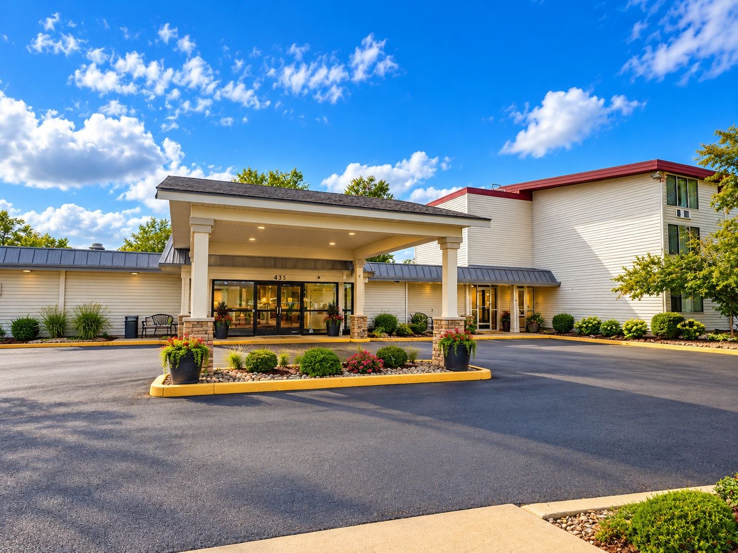 A hotel entrance with a covered walkway, a parking lot, and landscaped areas.