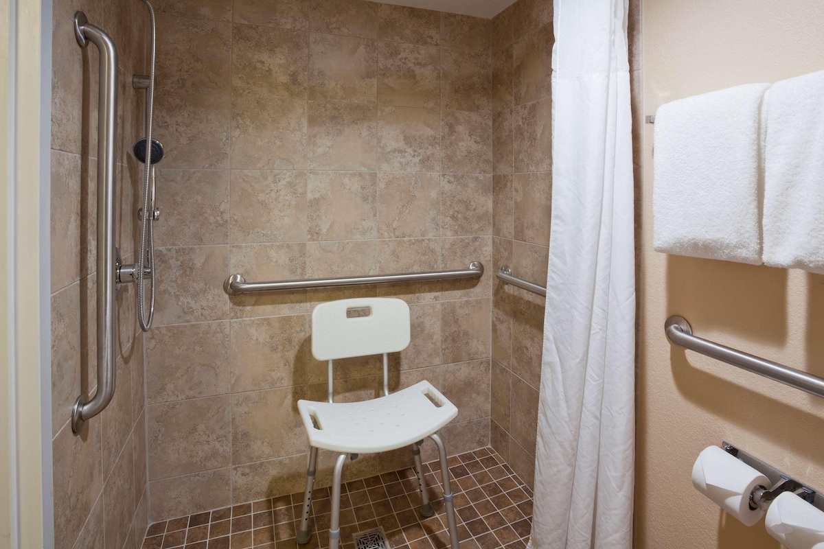 A shower area with a white chair, grab bars, and a towel rack.