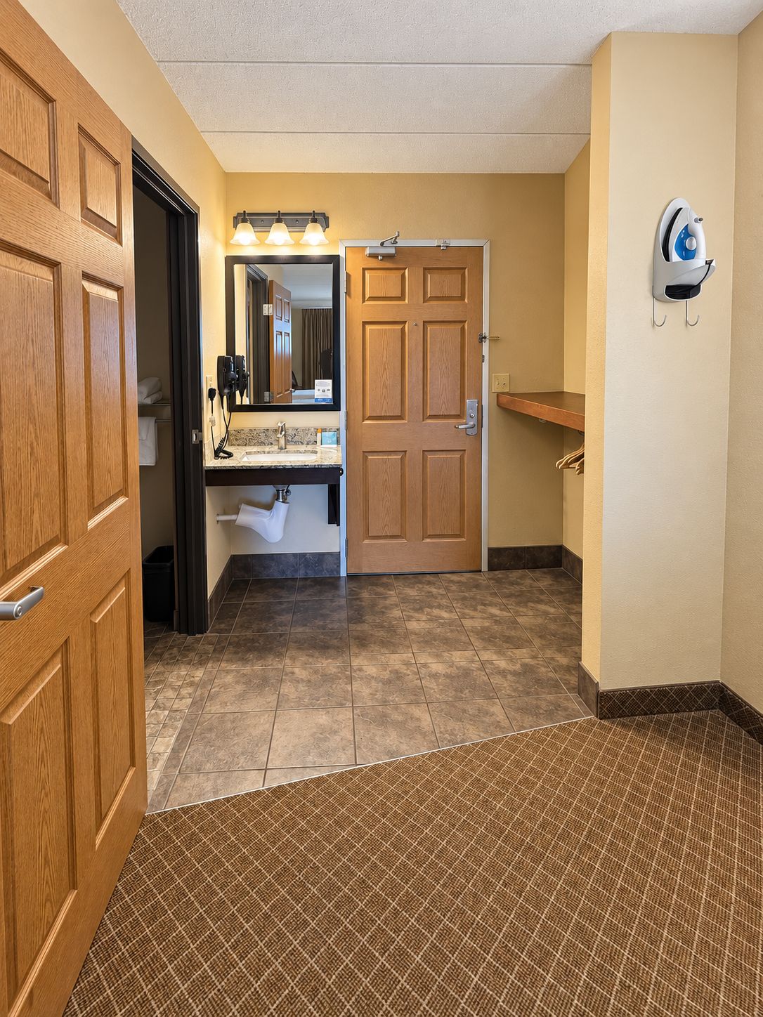 A hotel bathroom with a wooden door, a sink with a mirror, and a towel rack.