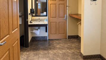A hotel bathroom with a wooden door, a sink with a mirror, and a towel rack.