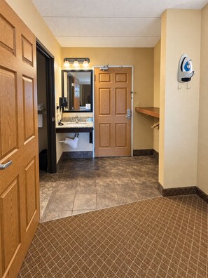 A hotel bathroom with a wooden door, a sink with a mirror, and a towel rack.