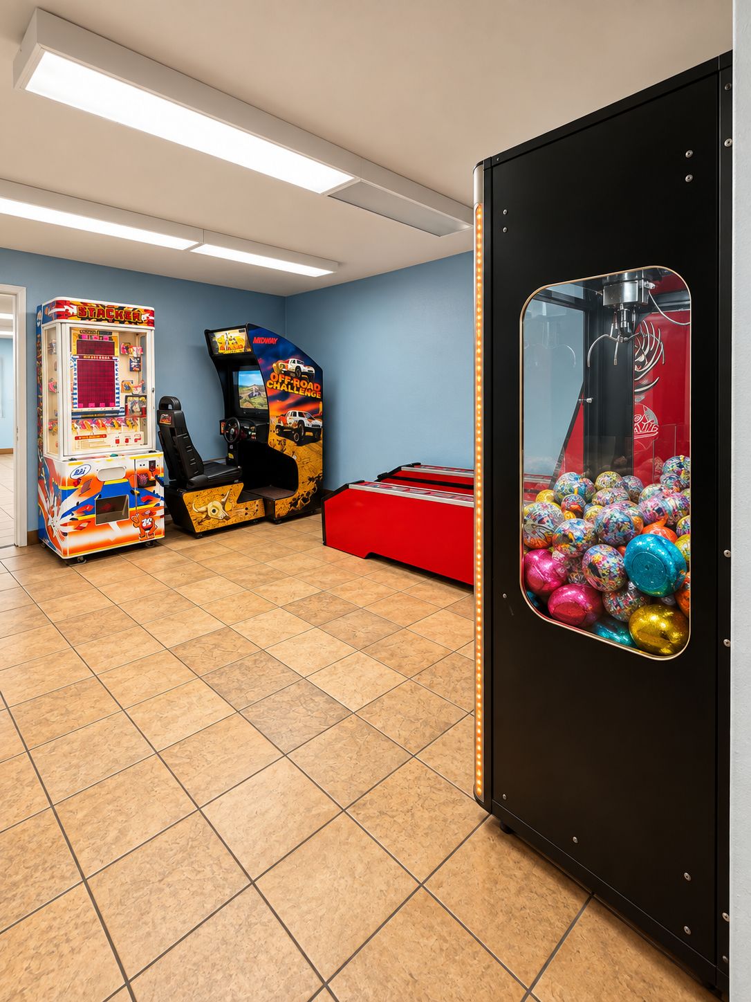A room with arcade games, a claw machine, and a red play table.