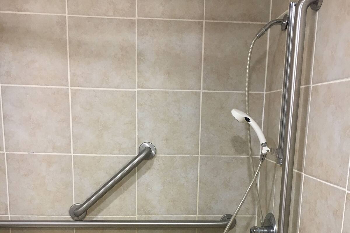 En duschplats med ett stödhandtag, ett duschhuvud som kan hållas i handen och en vit stol.