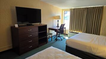 Une chambre d’hôtel avec un lit, un bureau et une chaise, une télévision posée sur une commode, et une fenêtre avec des rideaux.
