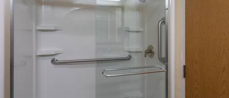 Une cabine de douche fermée par des parois en verre, équipée d’une barre d’appui en métal et d’un pommeau de douche.