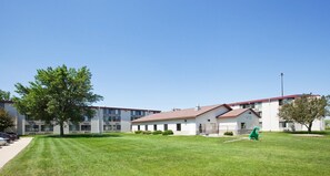 A multi-story building with a flat roof, a grassy courtyard, and a statue.