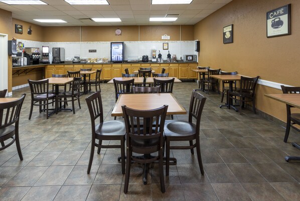 A café with multiple tables and chairs, a kitchen area with appliances, and a clock on the wall. - Med City Inn & Suites - Mayo Clinic Area (Rochester)