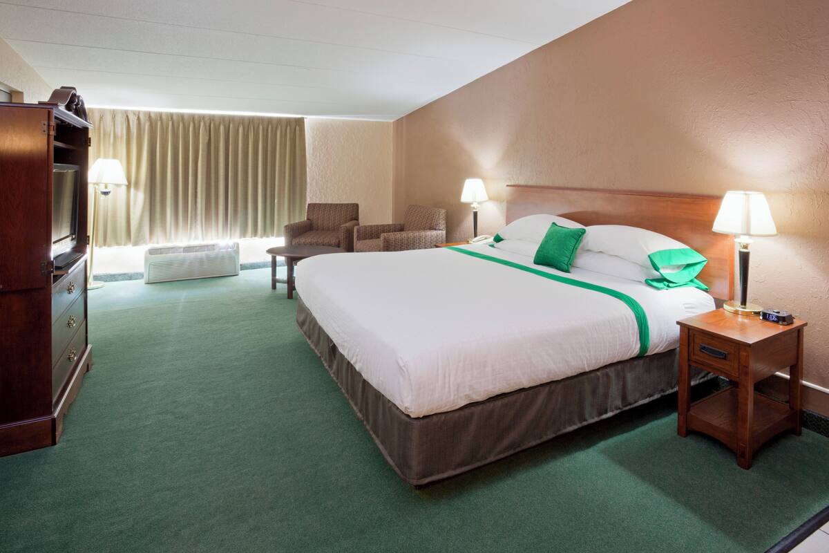 Ett hotellrum med en stor säng, ett skrivbord, en stol, en TV och en lampa.