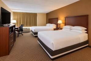 A hotel room with two beds, a desk, a chair, a television, and a lamp.