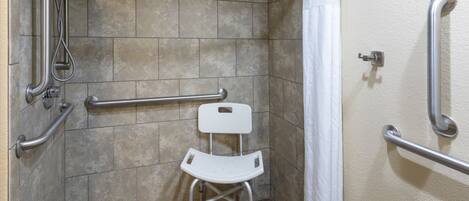Un espace douche équipé de barres d’appui, d’une chaise blanche et d’un pommeau de douche.