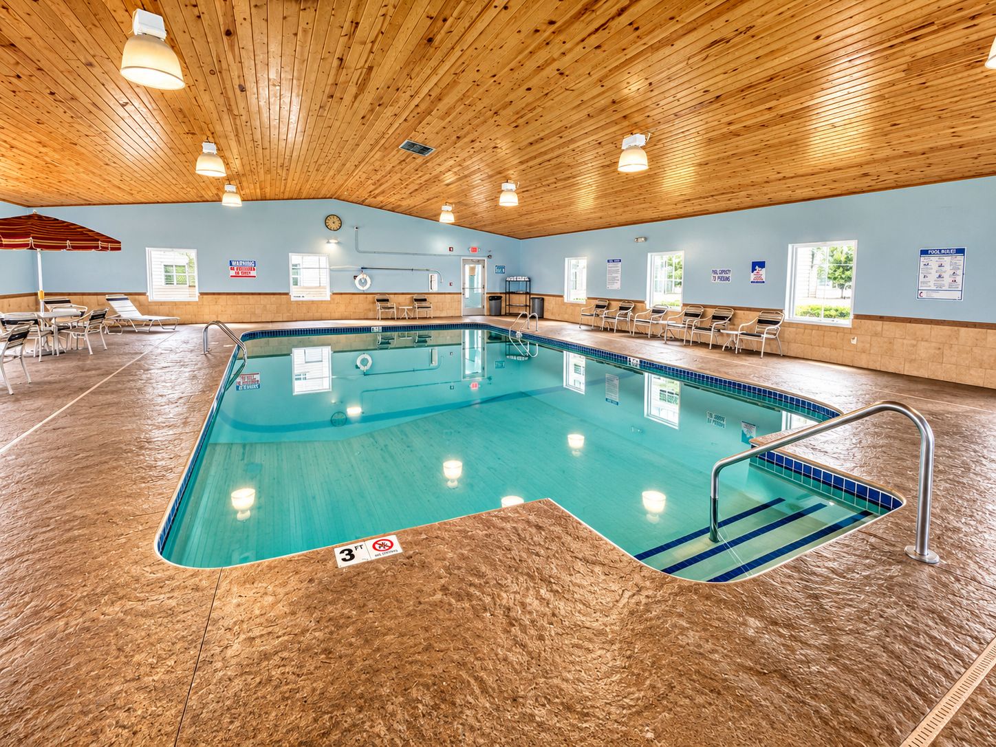 Ein Innenpool mit Holzbalkendecke, übersichtlichem Poolbereich und Liegestühlen.