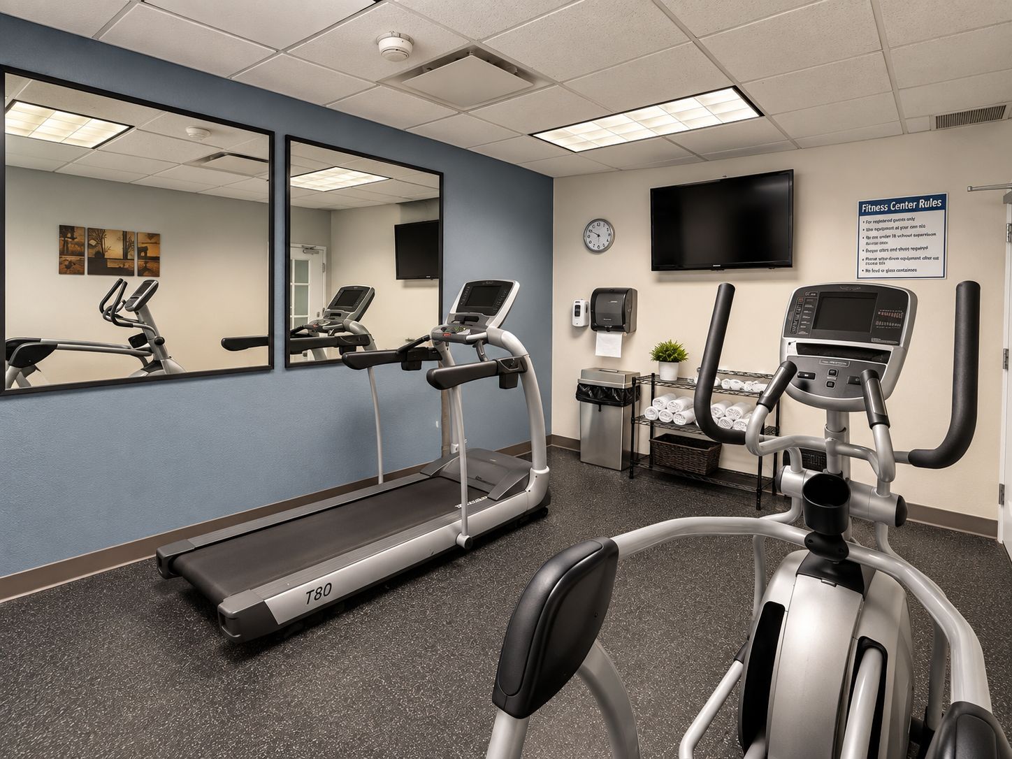 Ein Fitnessstudio mit Laufbändern, Crosstrainern und einem an der Wand befestigten Fernseher.