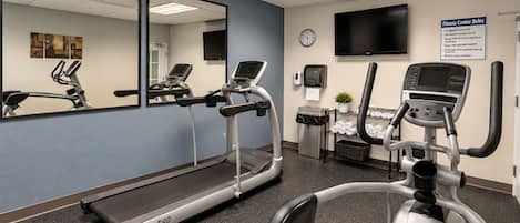 Ein Fitnessstudio mit Laufbändern, Crosstrainern und einem an der Wand befestigten Fernseher.
