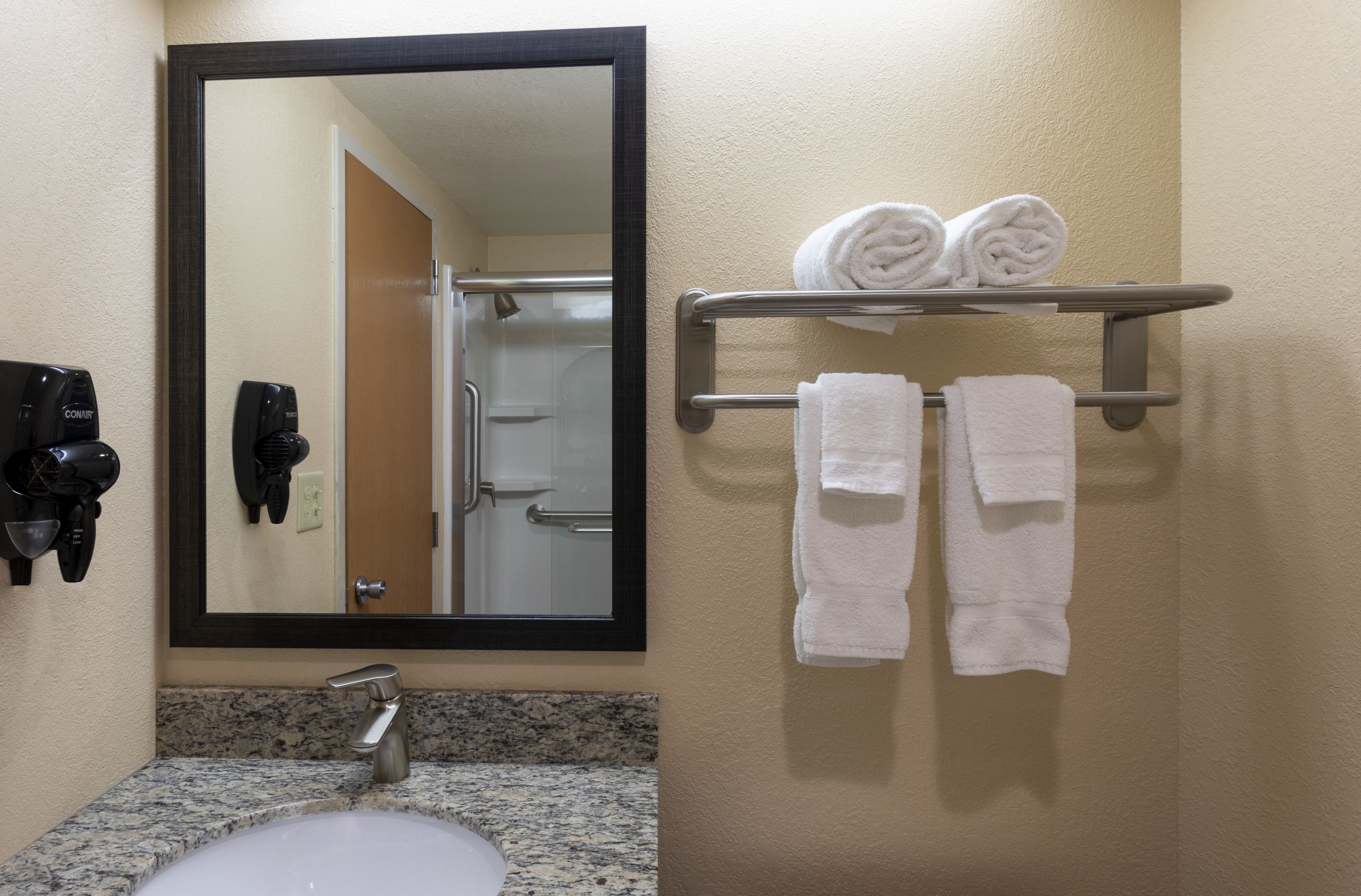Un baño con lavamanos, espejo, toallero y secadores de pelo.