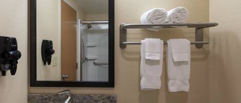 Un baño con lavamanos, espejo, toallero y secadores de pelo.