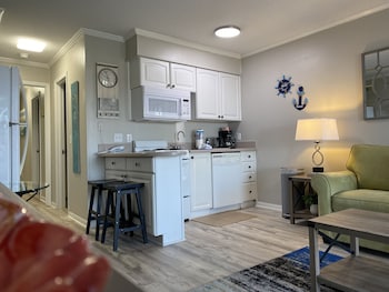 A living room with a beige sofa, two red armchairs, a coffee table with a vase of flowers, and a kitchen in the background. at Hilton Head Island Beach & Tennis Resort