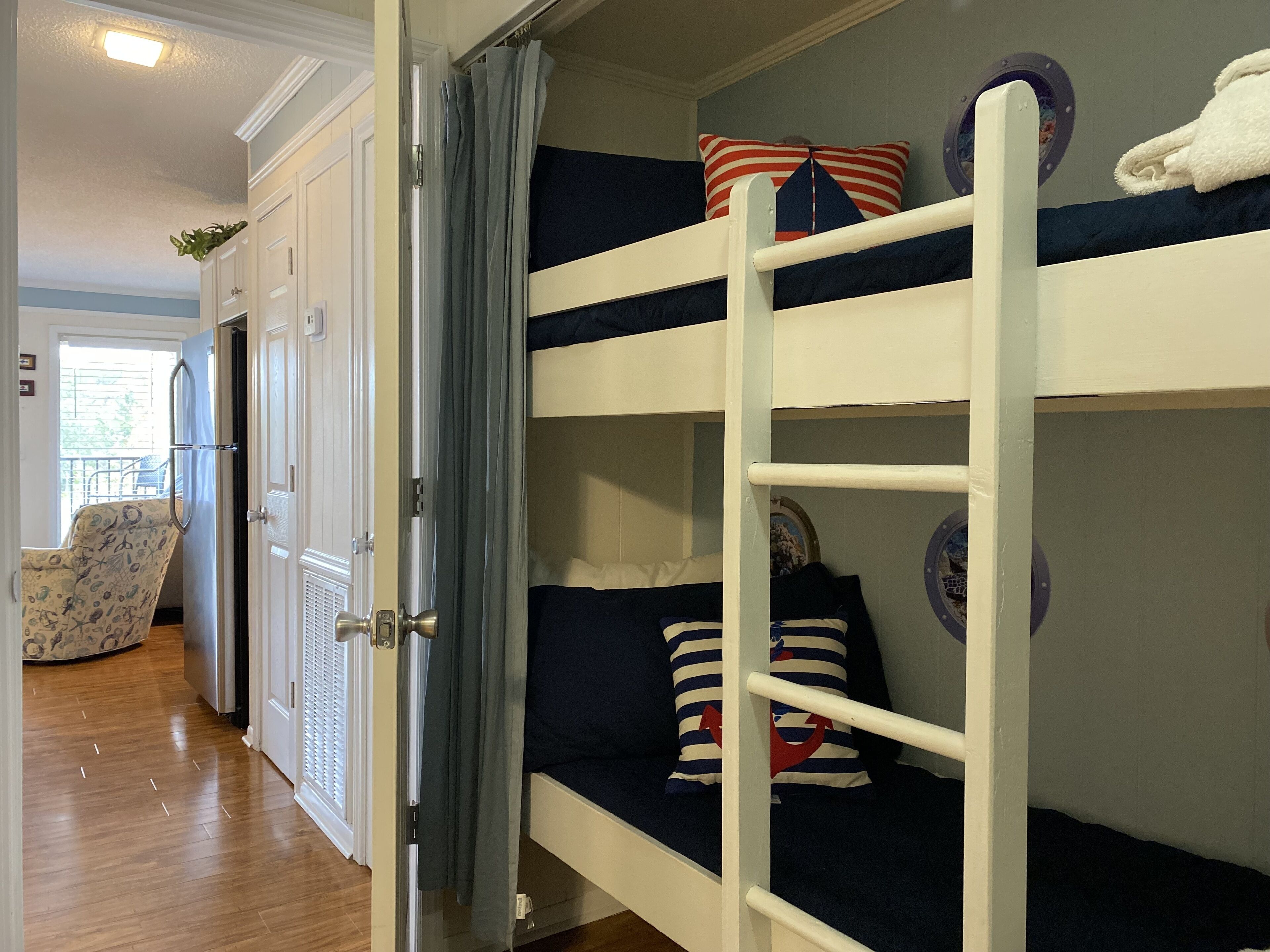 Ein Stockbett mit dunkelblauer Bettwäsche und gestreiften Kissen, eine weiße Tür und ein Stuhl mit Blumenmuster.