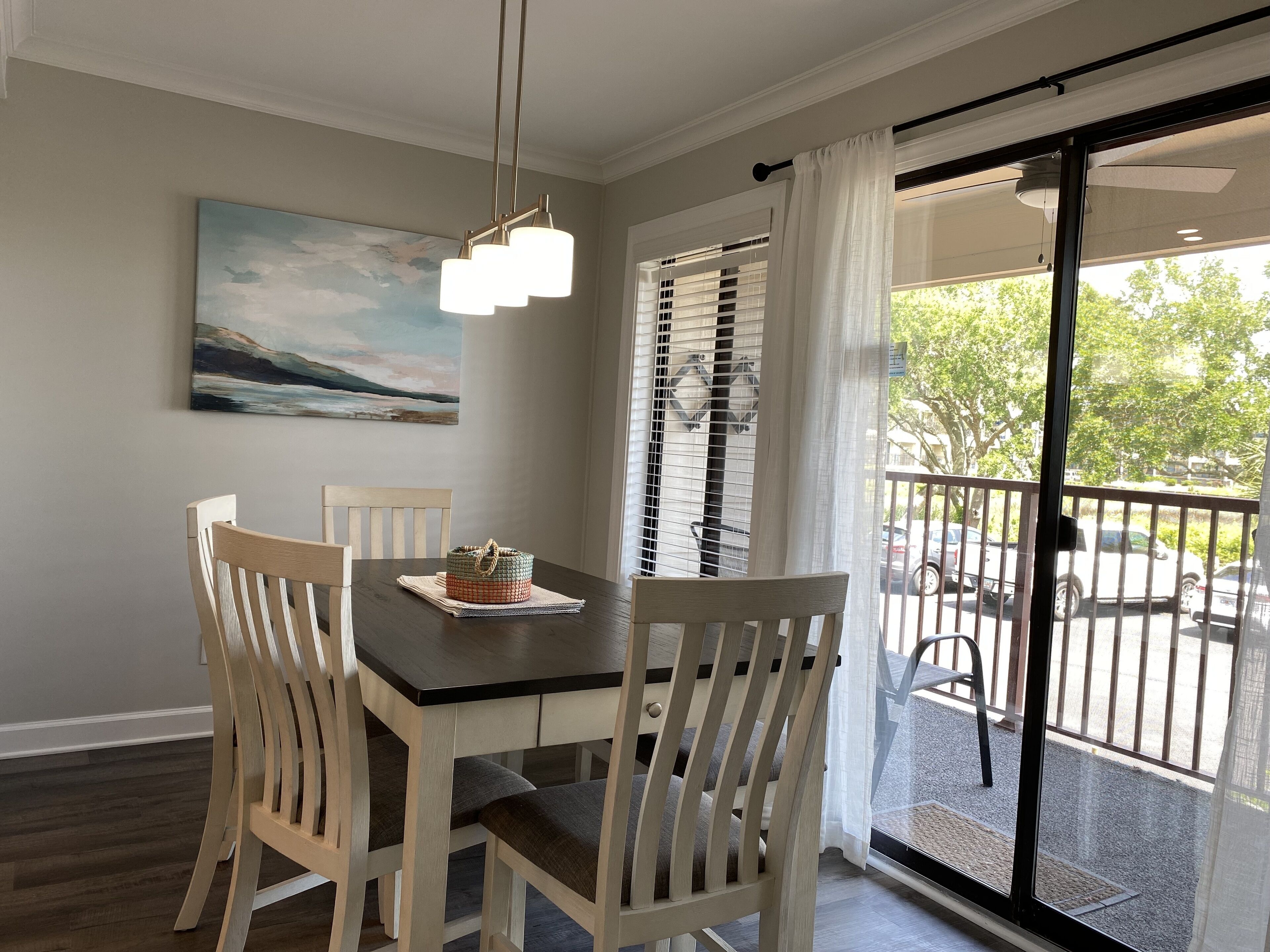 A dining area with a table, chairs, a painting, and a view through a window.