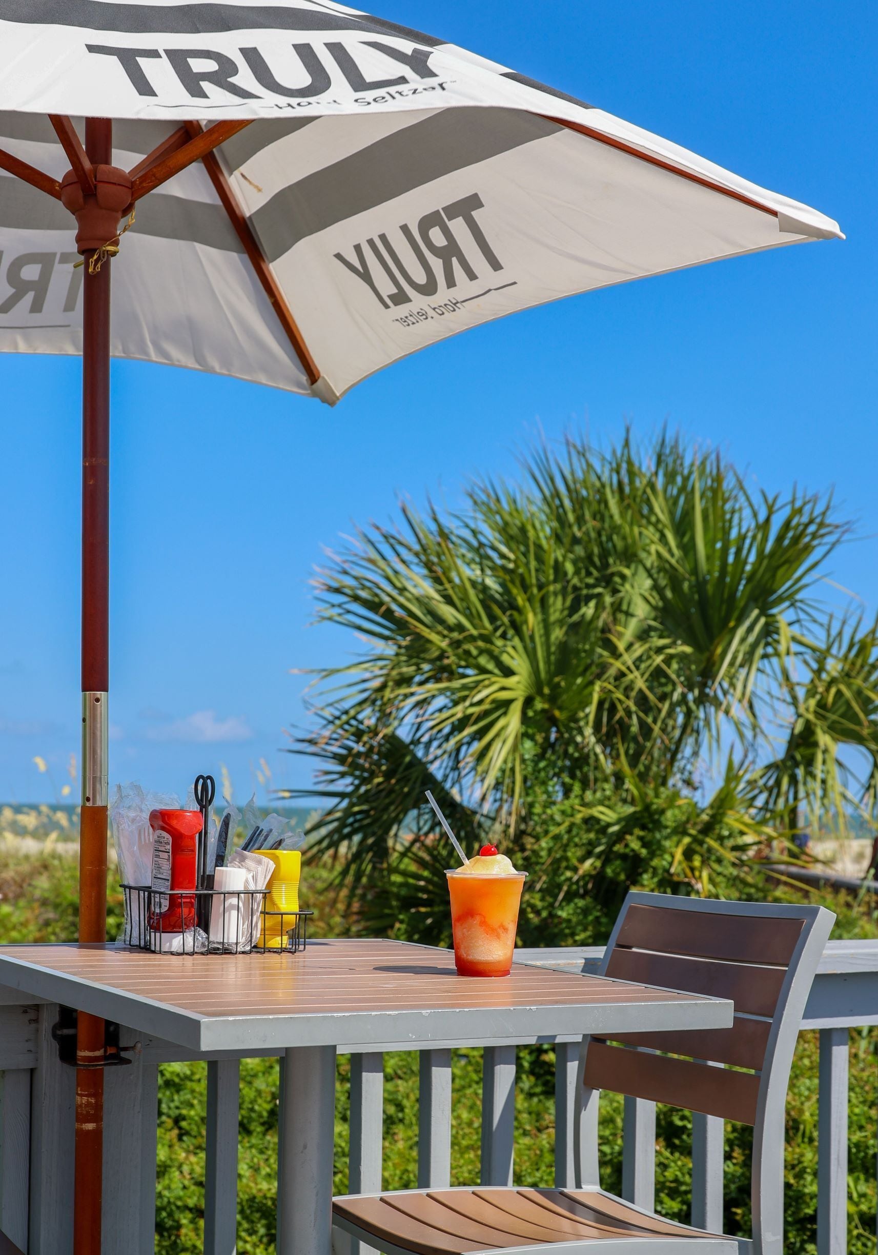 An outdoor table with a white umbrella labeled "TRULY" and a drink.