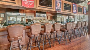 Un espace bar doté de comptoirs en bois, de nombreux tabourets et de bannières affichant les réalisations des équipes de football de l’Ohio State et des New York Giants.