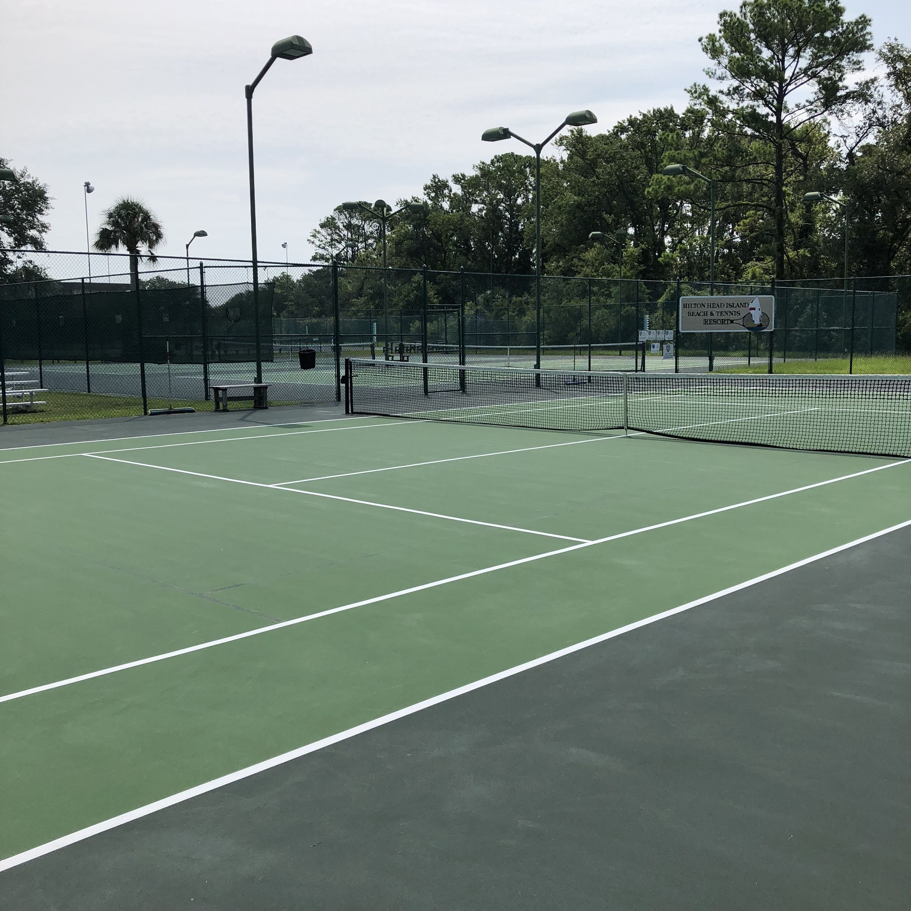 Pista de tenis con red, bancos y un letrero para el Resort Playa y Tenis de Hilton Head Island.