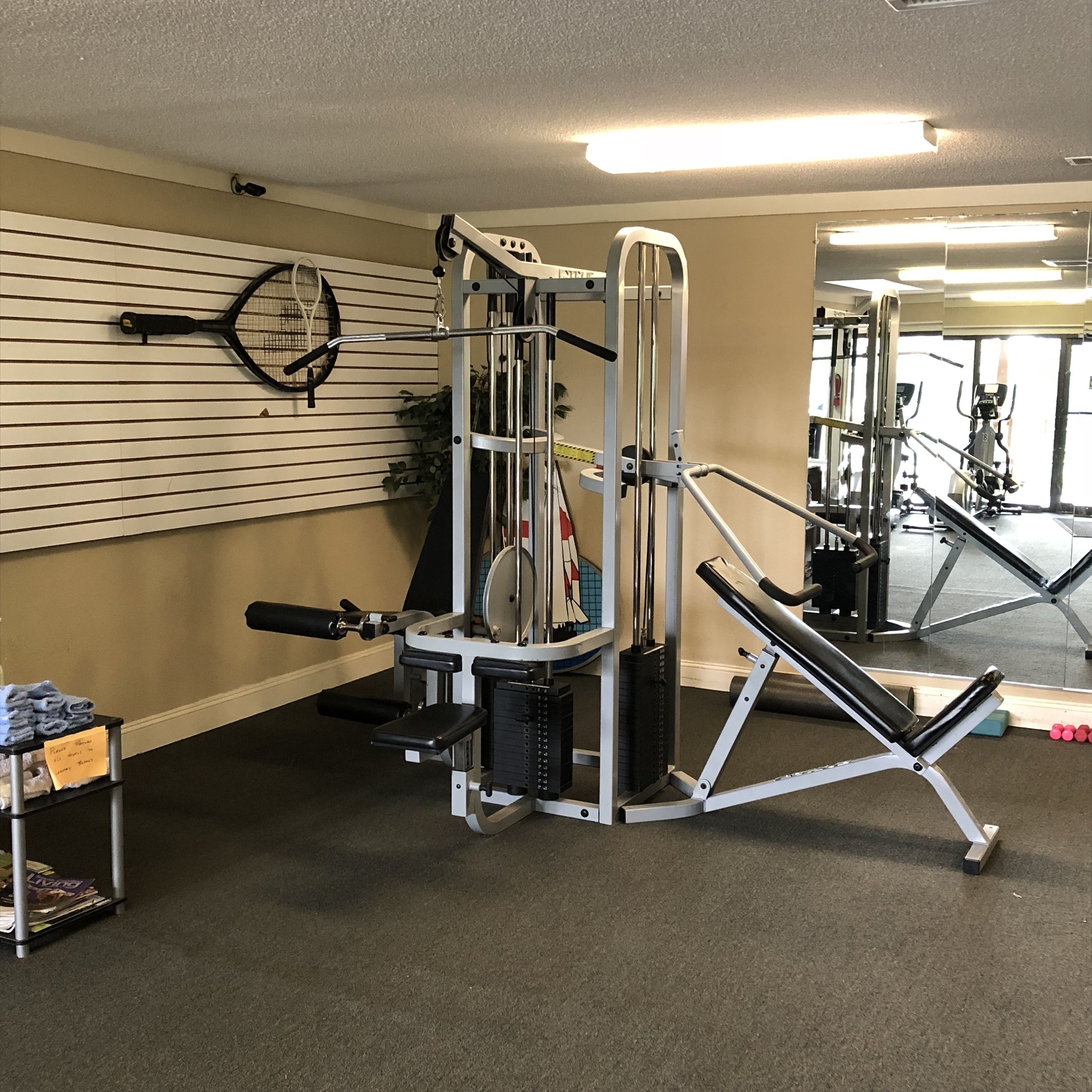 A gym with exercise equipment, a wall-mounted mirror, and a small table with towels.