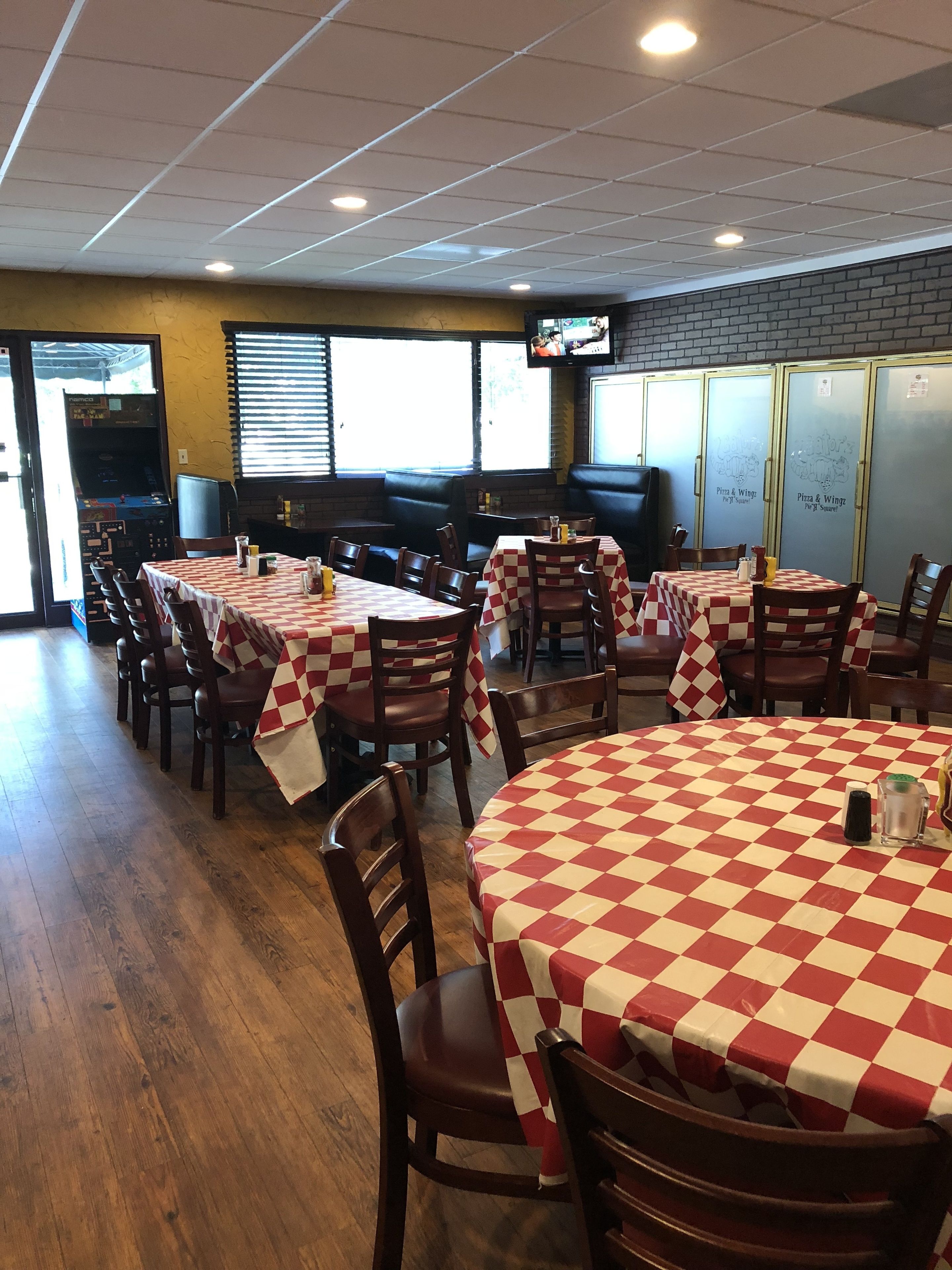 A restaurant interior with multiple tables covered in checkered tablecloths, wooden chairs, and a brick wall.