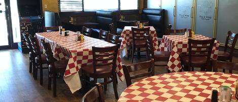 A restaurant interior with multiple tables covered in checkered tablecloths, wooden chairs, and a brick wall.