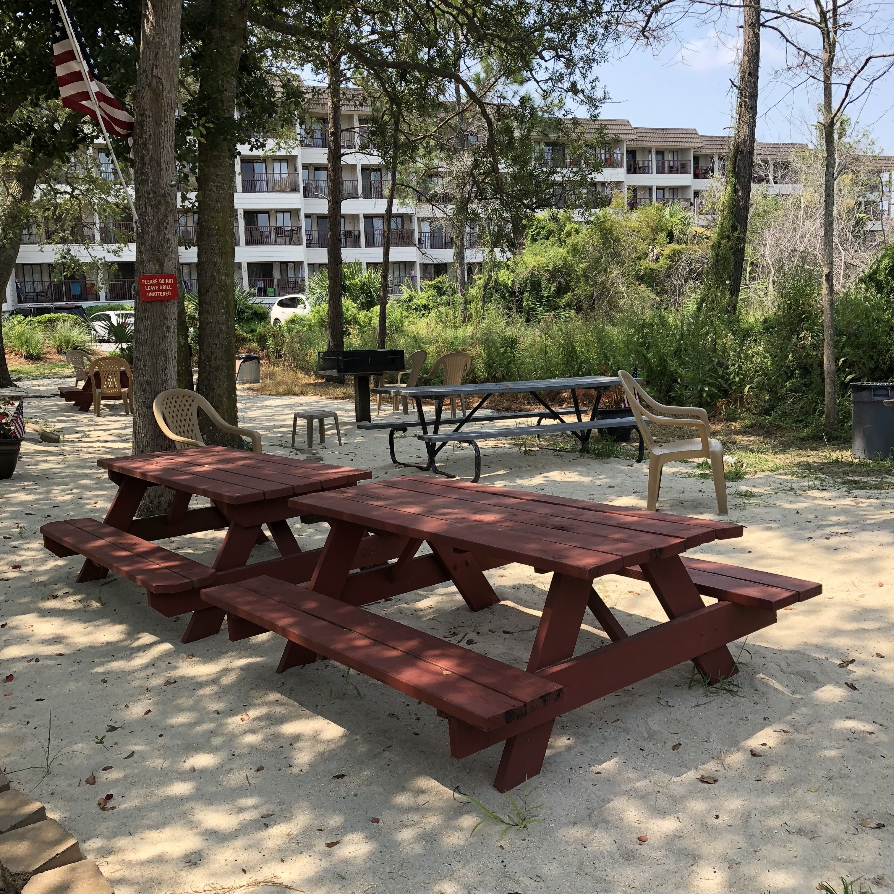 Ein Picknickplatz mit roten Picknicktischen und Stühlen, umgeben von Bäumen und einem Gebäude im Hintergrund.