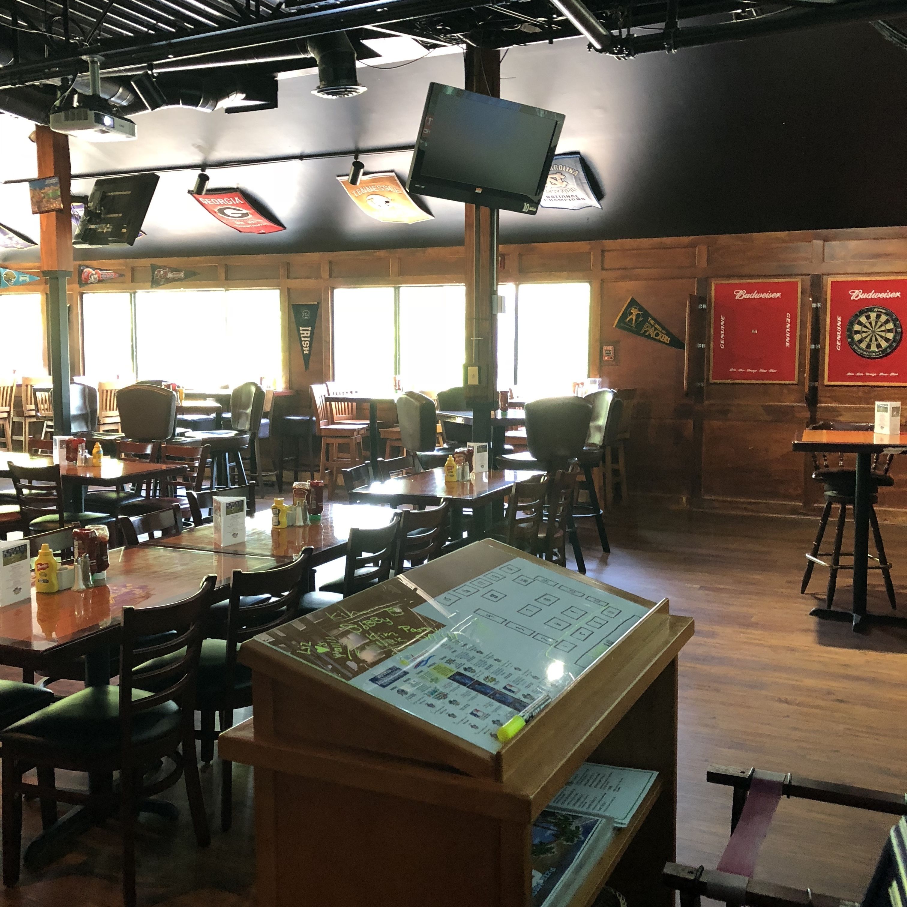 A restaurant with multiple tables and chairs, a menu stand, and a large screen.