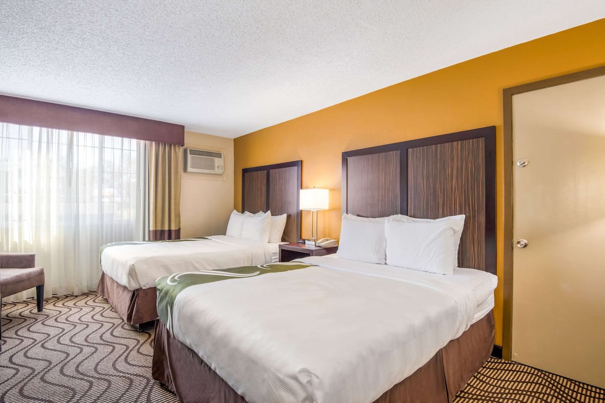 A hotel room with two beds, a desk, a chair, and a window with curtains.