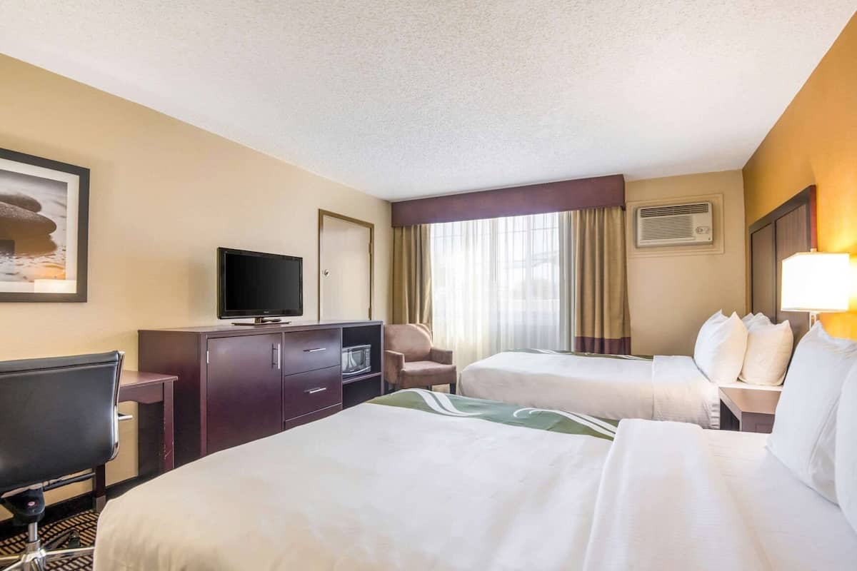 A hotel room with two beds, a television, a desk with a computer, and a window with curtains.