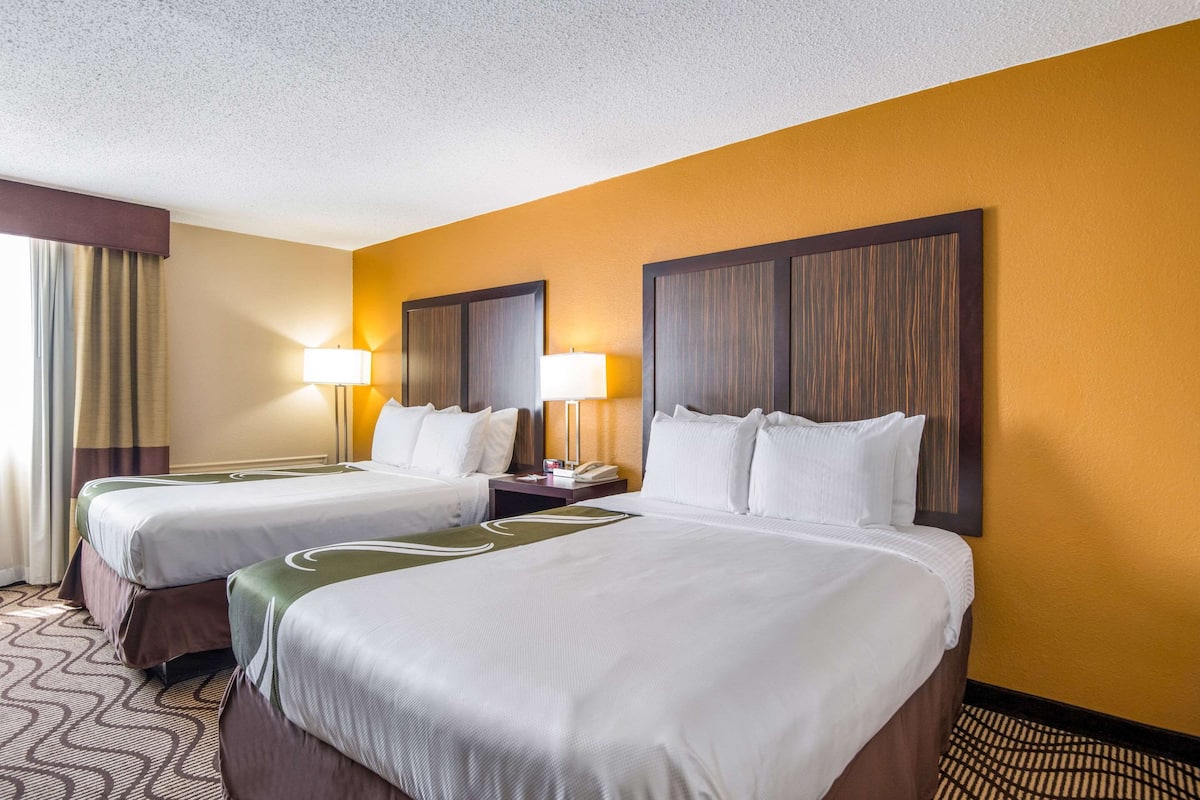 A hotel room with two beds, a nightstand with a lamp, and a large mirror on the wall.