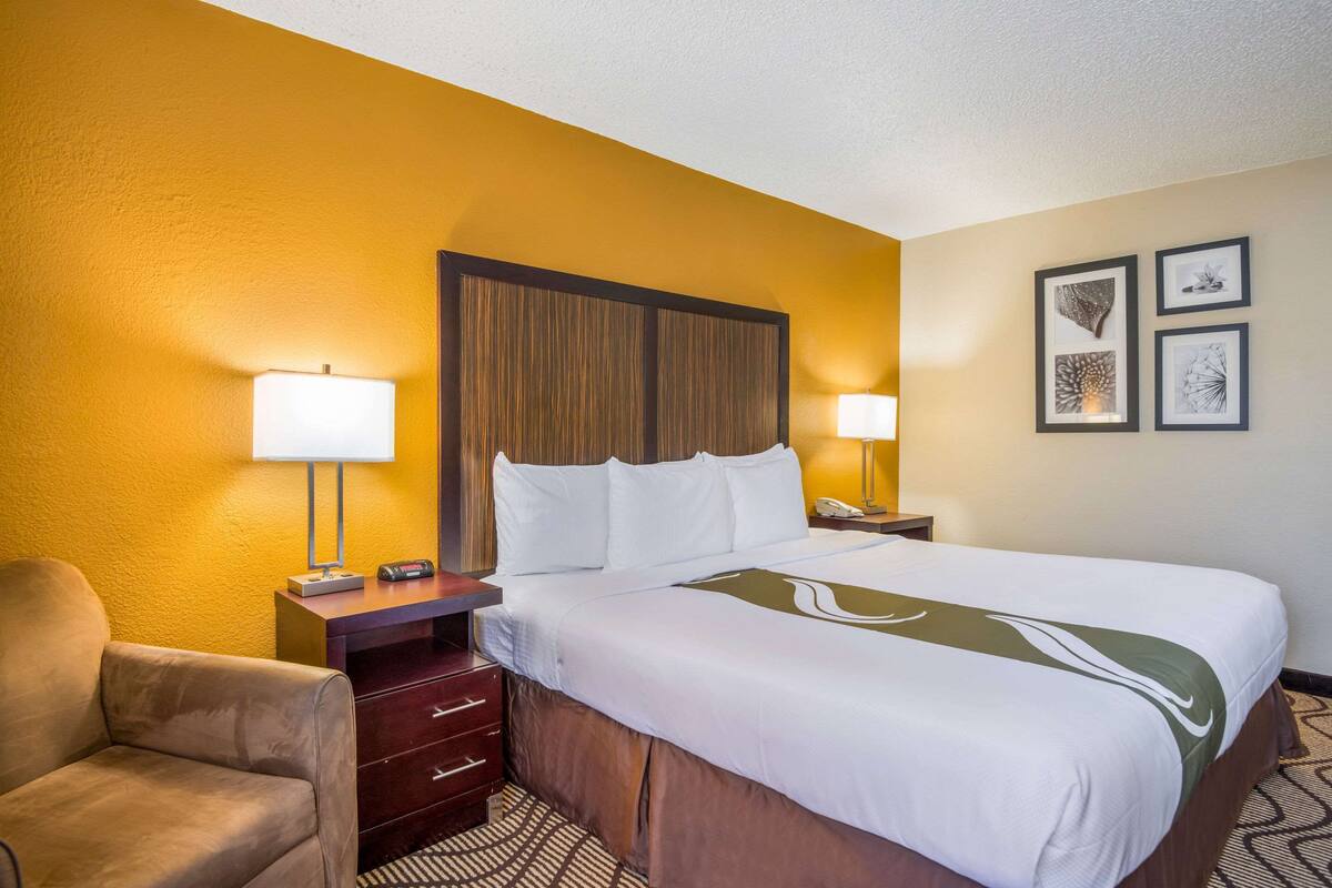 A hotel room with a bed, a desk, a chair, and artwork on the wall.