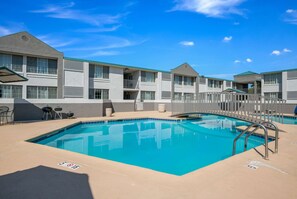A swimming pool with a clear blue water, surrounded by a beige deck.