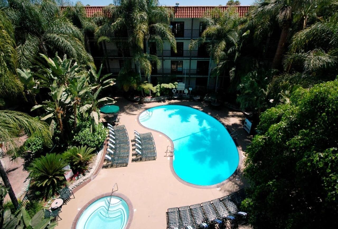 Un resort con una gran piscina central rodeada de palmeras y sillones de descanso.