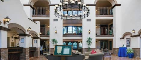Un hall d’entrée spacieux, agrémenté d’un grand lustre central, de plusieurs balcons et d’un comptoir de réception.