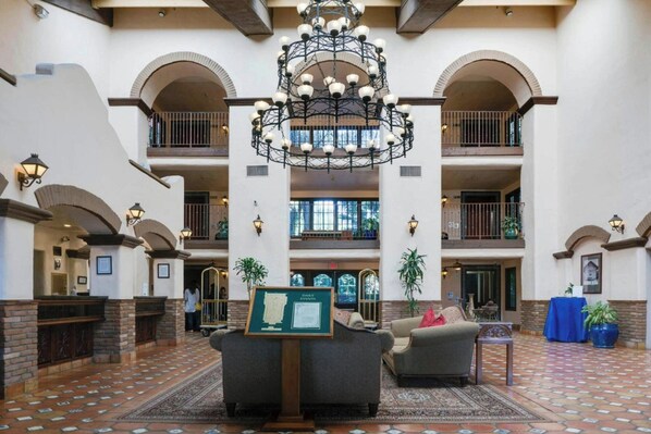 Un vestíbulo amplio con una lámpara central, varios balcones y un mostrador de recepción.