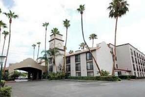 Entrada de hotel con un edificio moderno, palmeras y cielo despejado.