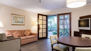 Una habitación con sofá, una mesa de comedor con sillas, un televisor y una ventana con persianas.
