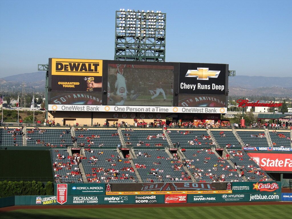 A baseball stadium with empty stands, advertisements for Chevrolet, Dewalt, and OneWest Bank, and a scoreboard displaying a game score.