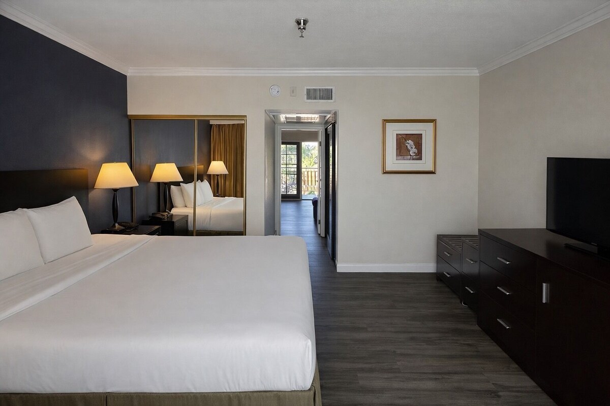 A hotel room with a large bed, bedside lamps, a television, a dresser, and a framed picture on the wall.