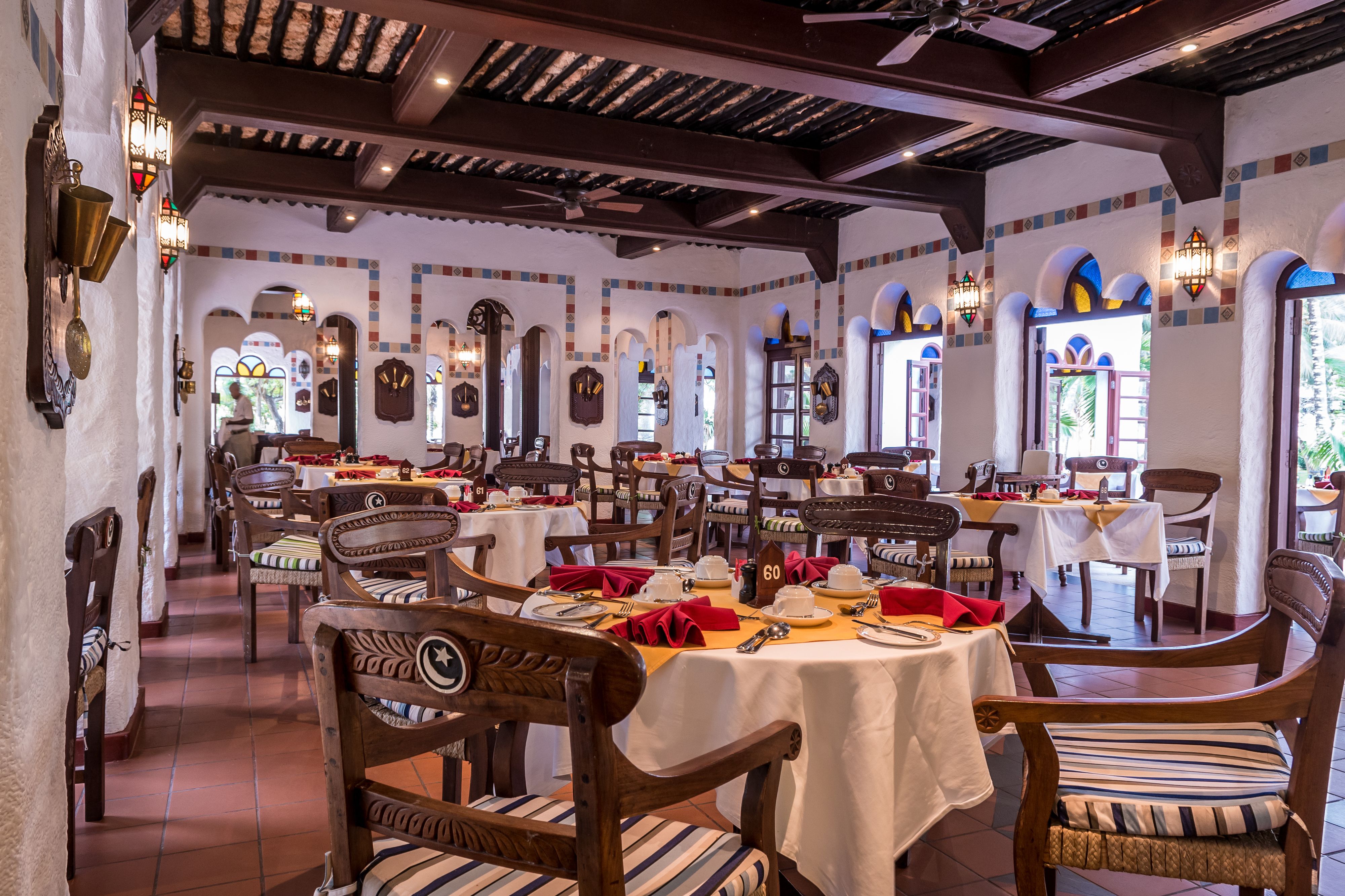 A restaurant with multiple tables set for dining, wooden chairs, and decorative wall sconces.