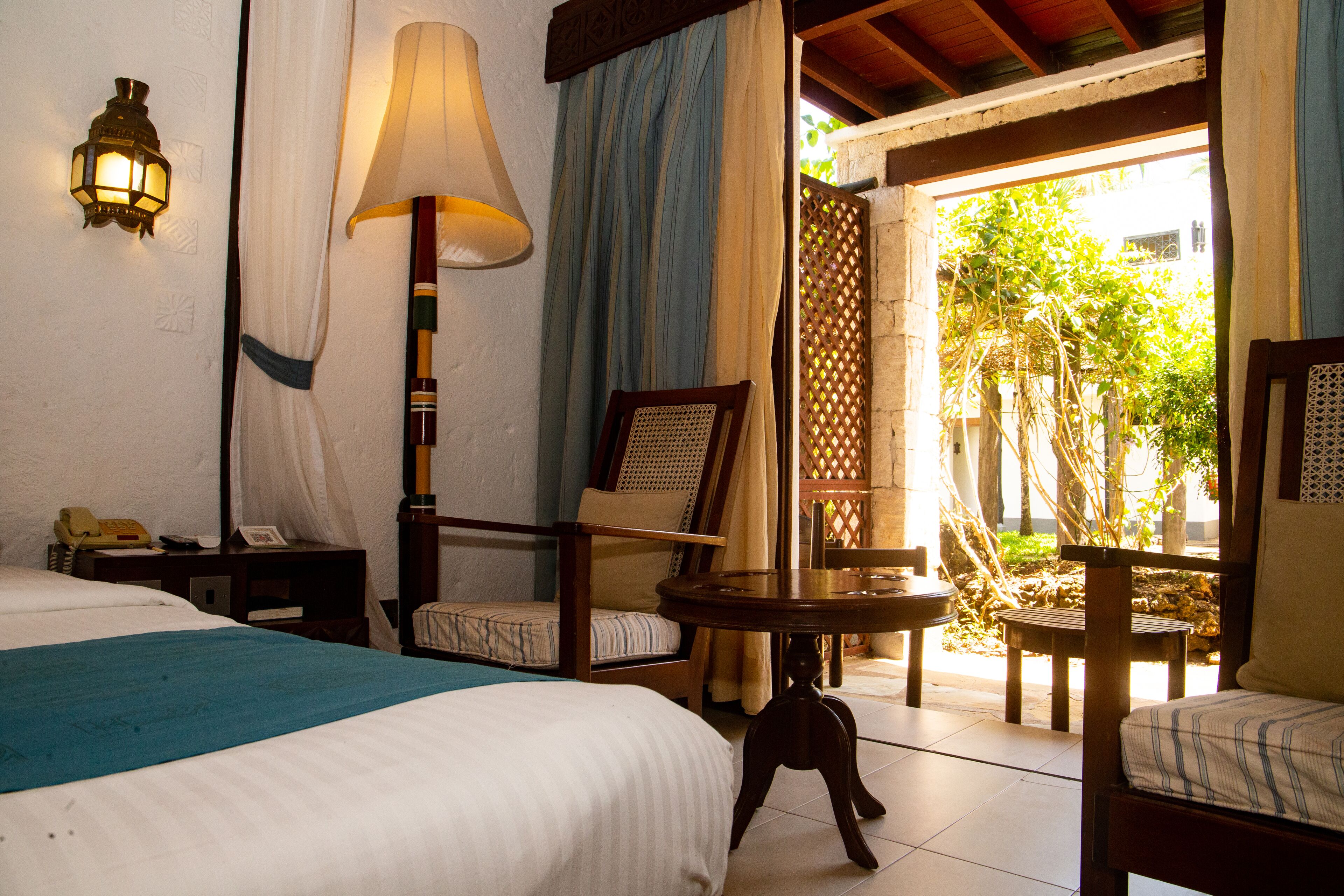 Una habitación de hotel con una cama, un escritorio con lámpara, una silla y una mesita.