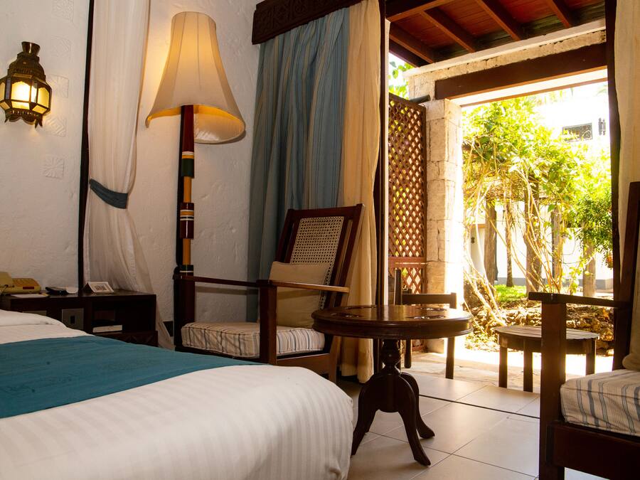 Una habitación de hotel con una cama, un escritorio con lámpara, una silla y una mesita.
