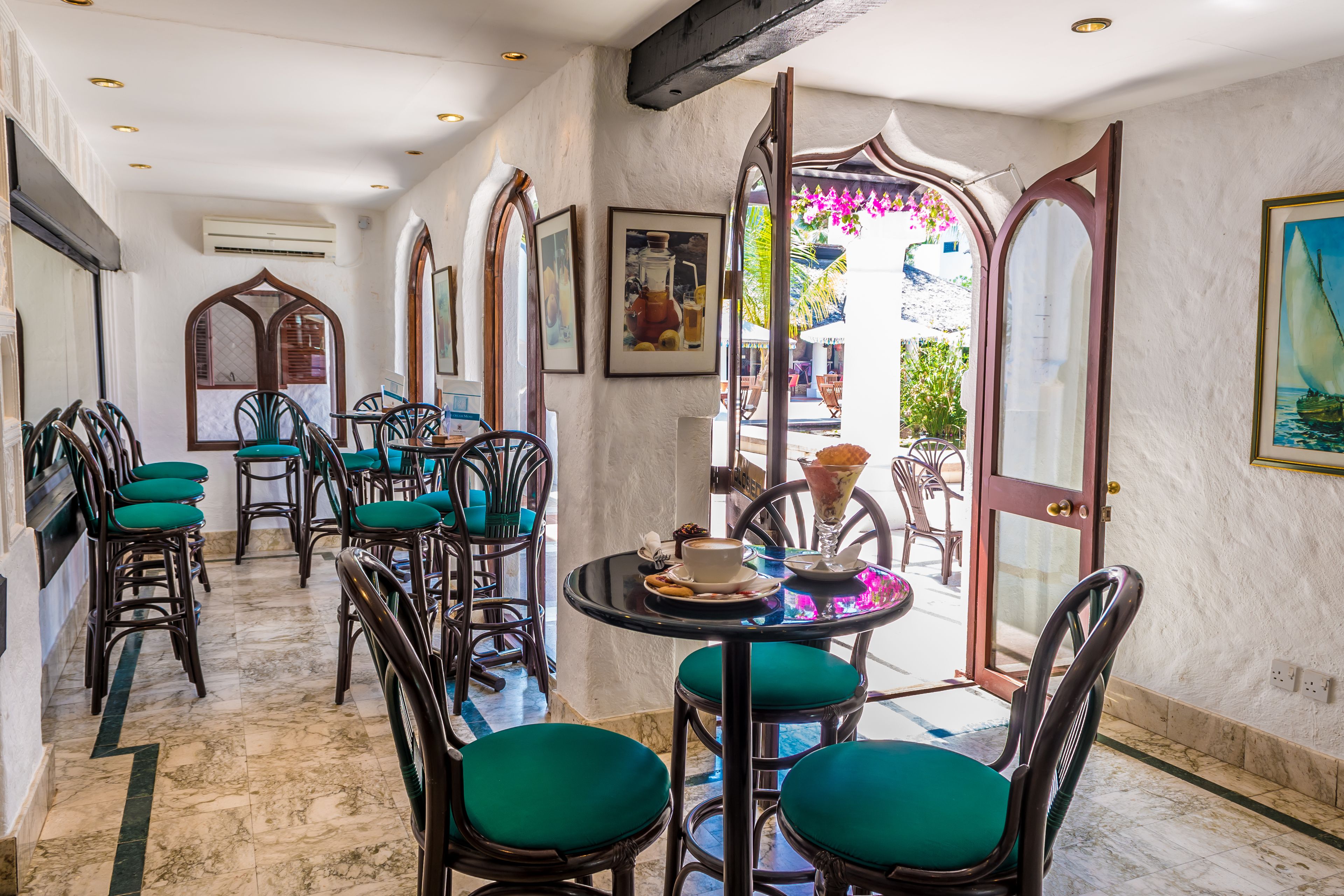 Un comedor con varias mesas y sillas, suelo de mármol y vistas al exterior.