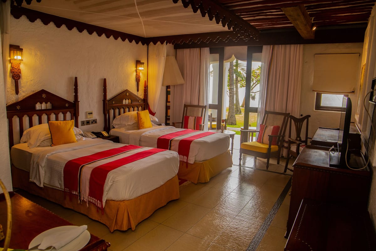 A hotel room with two beds, a desk, a chair, and a view of the outdoors.