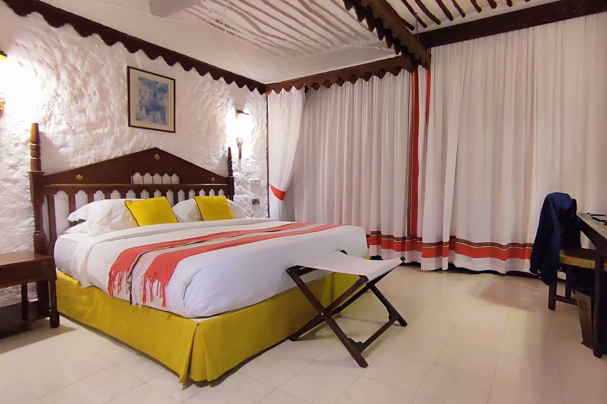 A hotel room with a bed, a desk, a chair, a lamp, and curtains.