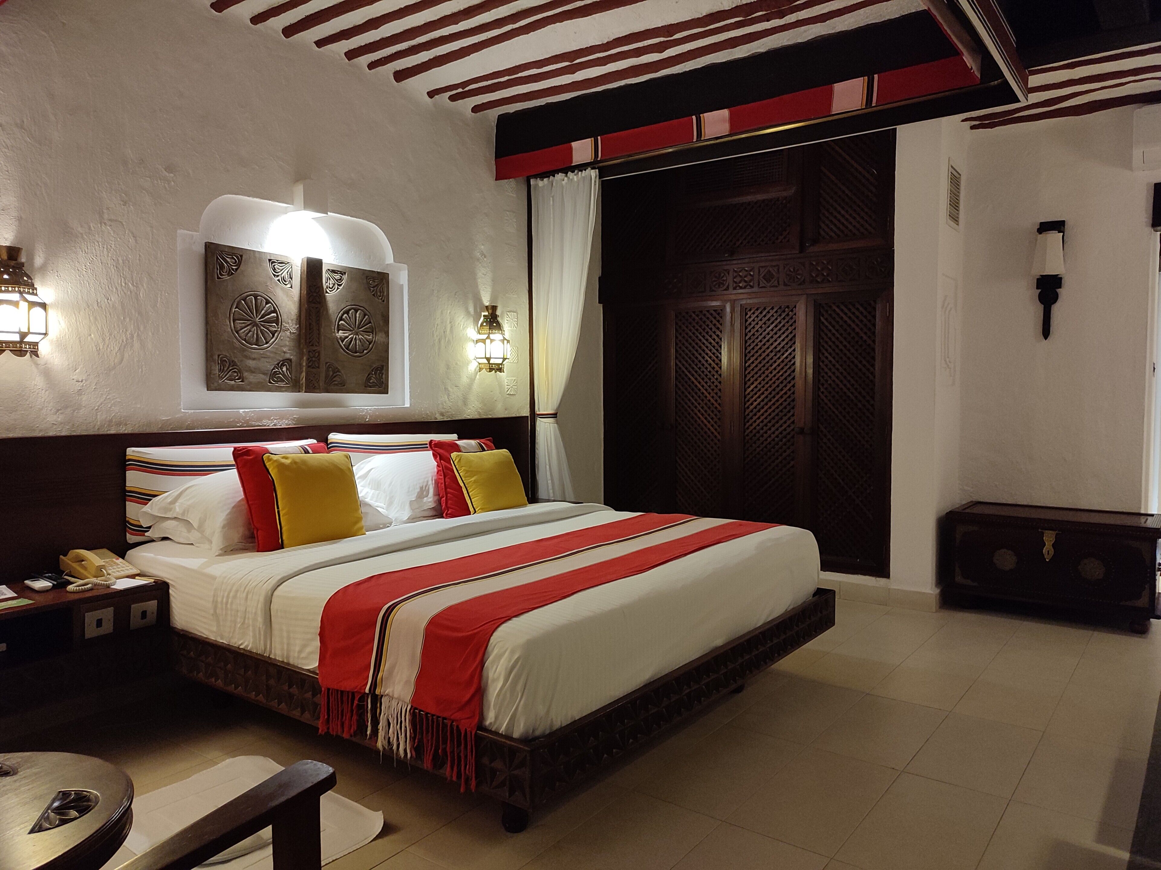A hotel room with a large bed, a nightstand, a bedside table, and a wardrobe.