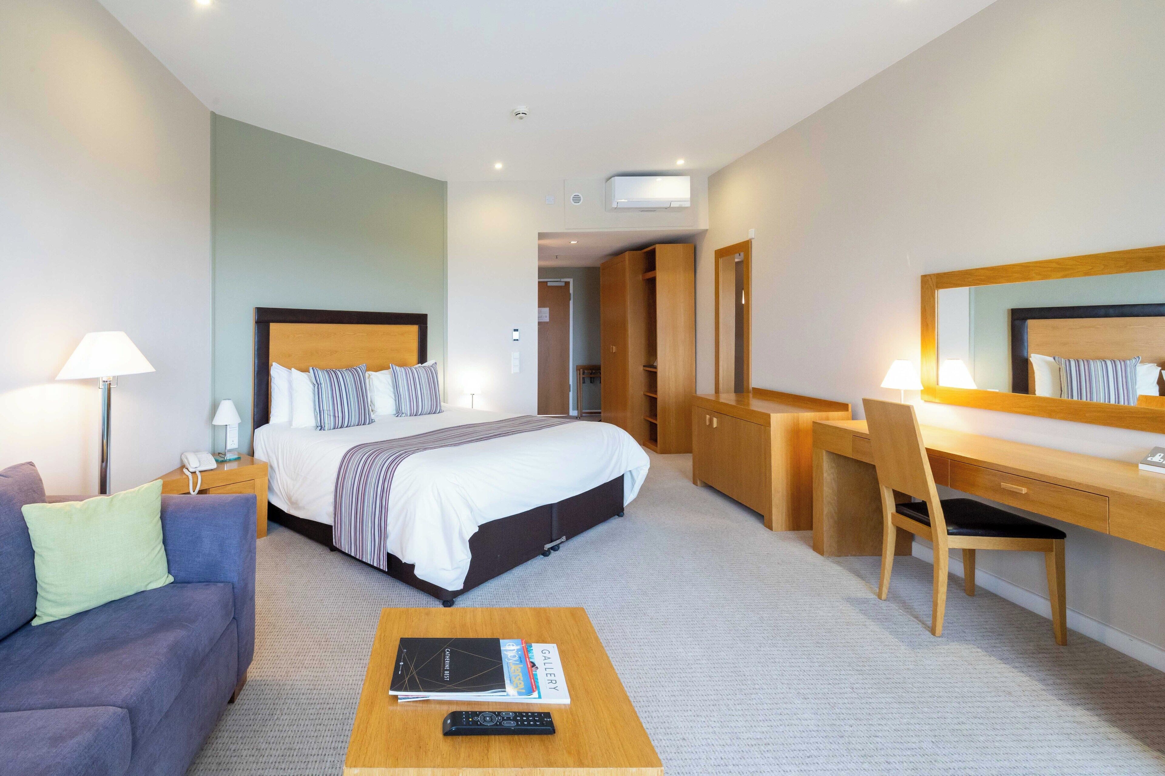A hotel room with a bed, a desk, a chair, a sofa, and a coffee table.